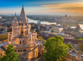 Golden summer sunrise with the tower of Fisherman's Bastion and green trees. Parliament of Hungary and River Danube