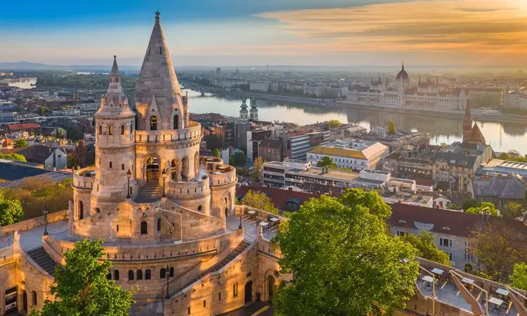 Golden summer sunrise with the tower of Fisherman's Bastion and green trees. Parliament of Hungary and River Danube